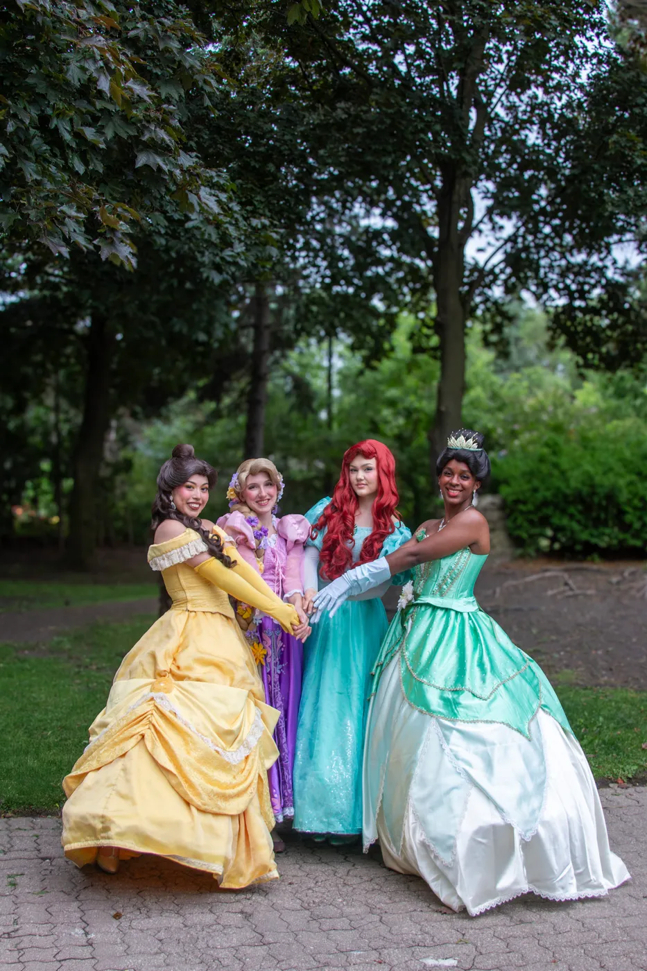 Belle, Rapunzel, Ariel and Tiana princesses holding hands in a garden